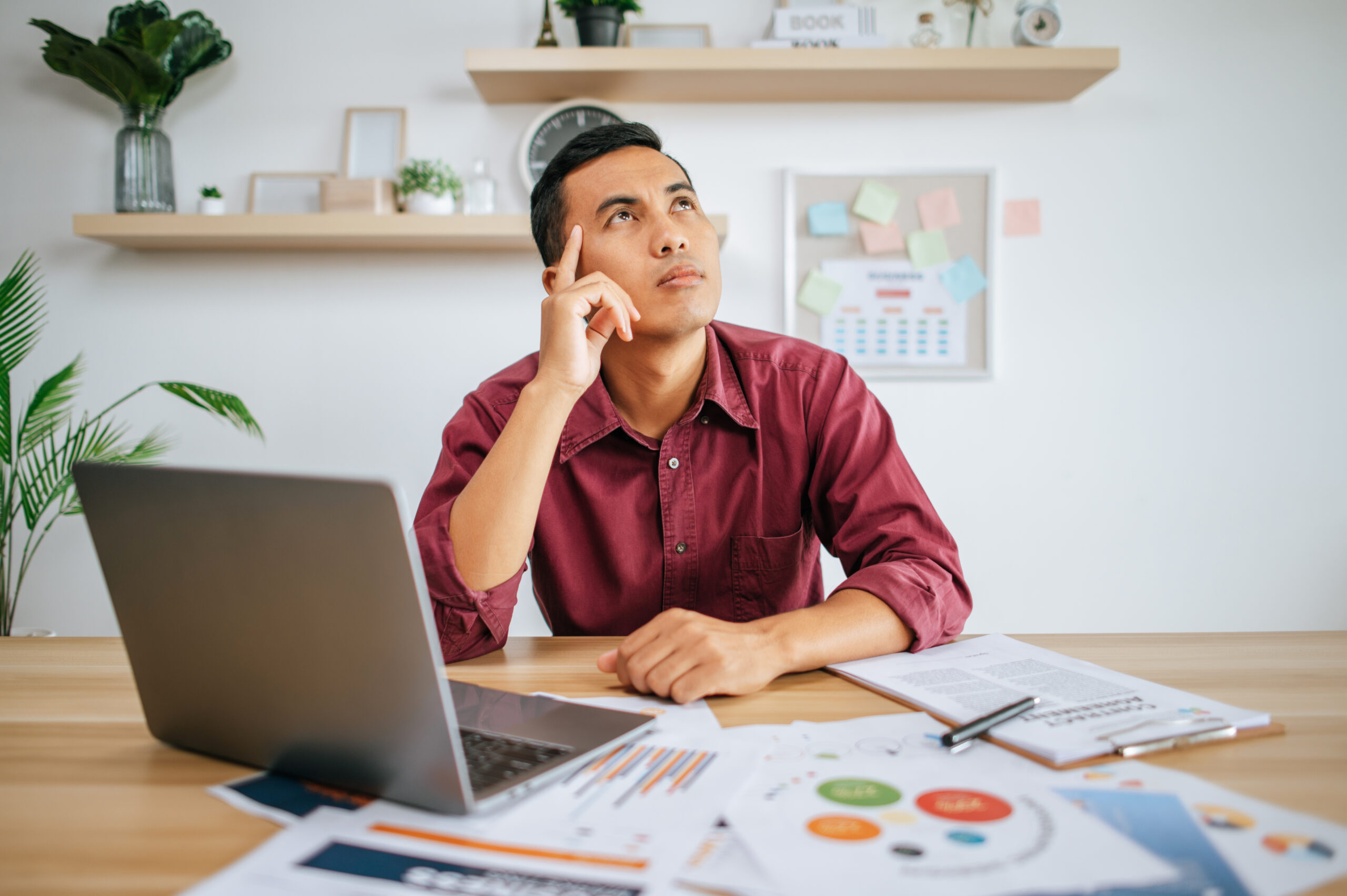 Man sitting at a desk with a laptop and documents, thoughtfully considering web development courses.